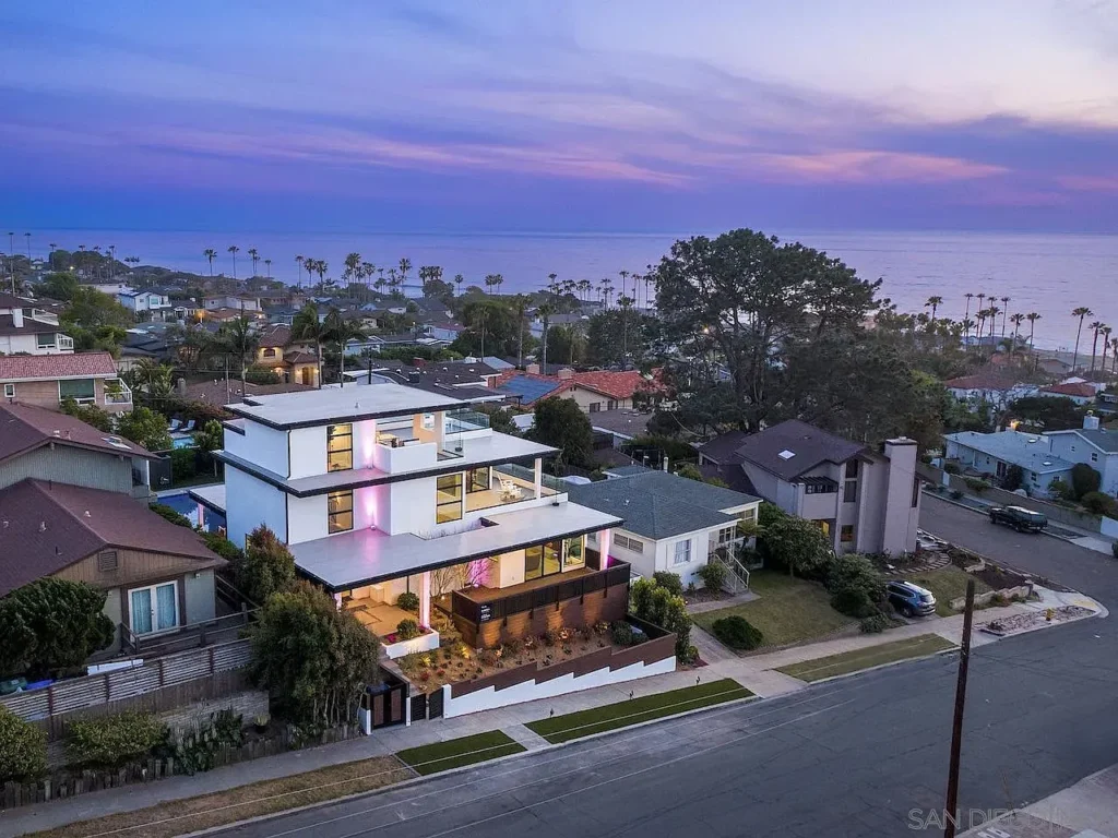 Aerial view of a house California real estate with palm trees and the ocean behind.