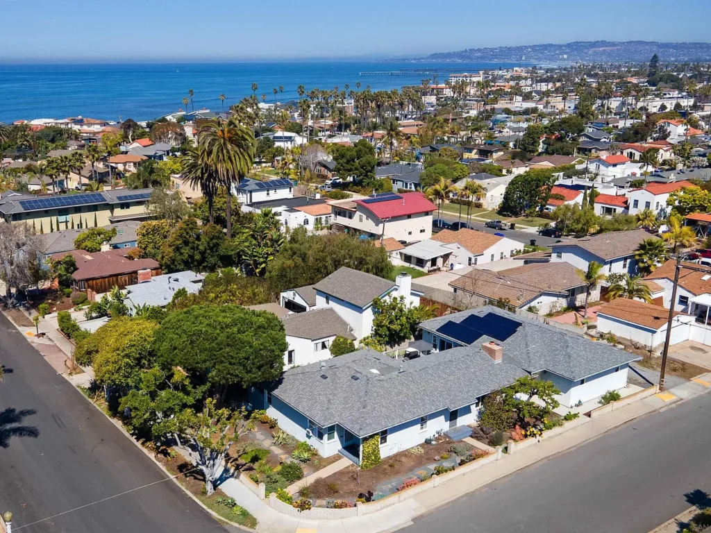 Aerial view of houses California real estate with palm trees and the ocean behind.