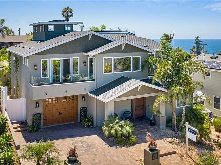 Two story house California real estate with gray walls, double garage, palm trees, and ocean view.