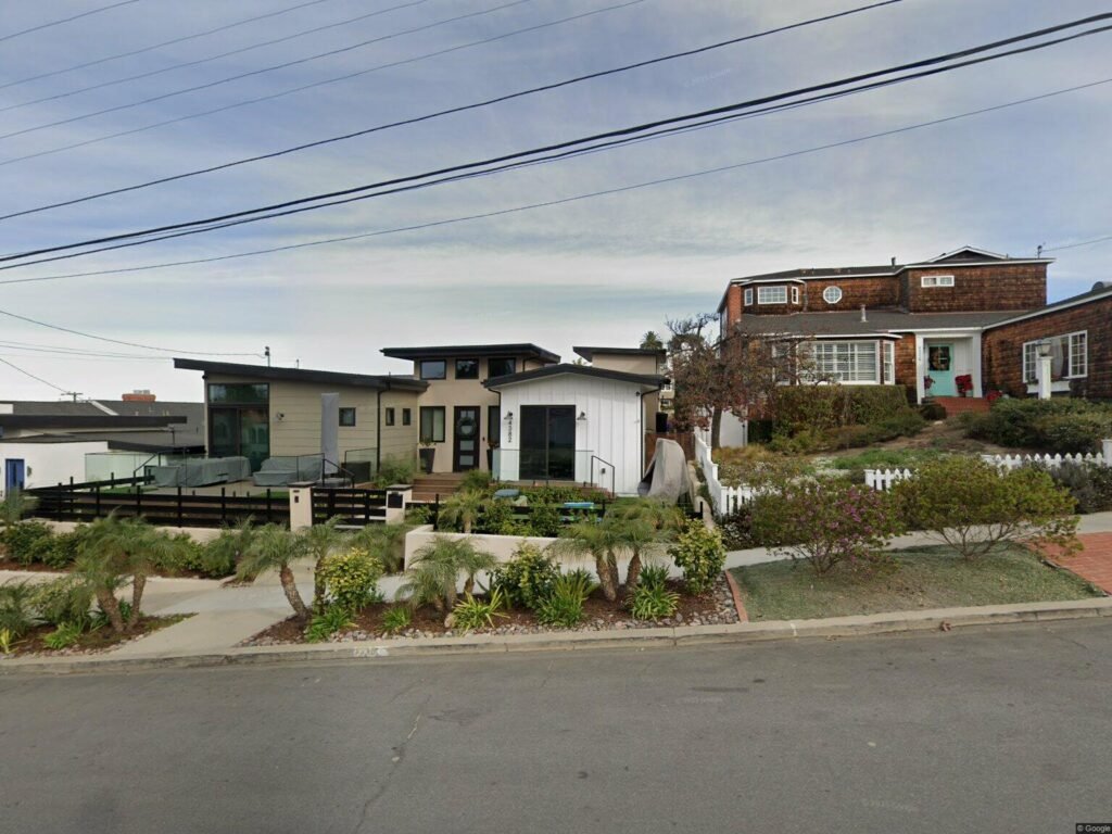 Street with homes California real estate and green plants by the sidewalk.