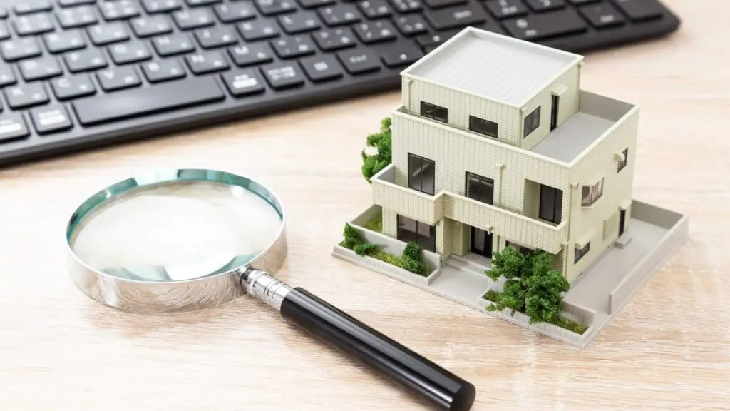 Magnifying glass and small house model on a desk with a keyboard.