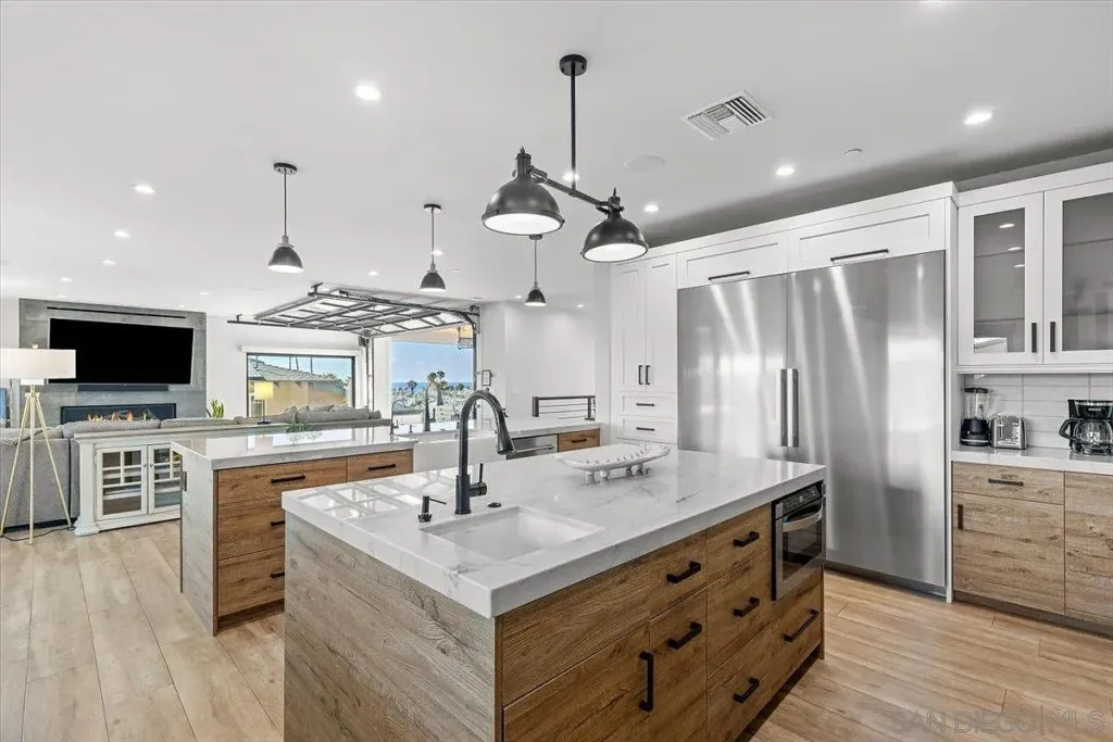 Kitchen with big island, stainless steel appliances, pendant lights, and wood floor.